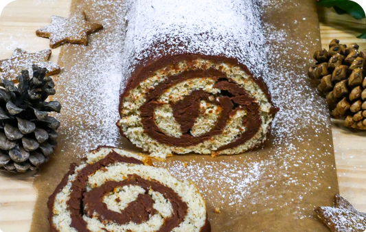 Bûche de noël à la farine de drêche blonde et au chocolat coupé avec des sablés en étoile sur le dessus, sur une assiette en marbre noir 